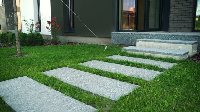 Modern stepping stone path leading to the entrance of a contemporary residential house through a green lawn, showcasing exterior design and landscape architecture