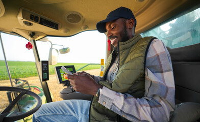Fototapeta premium Afro American farmer checking information on a smartphone while operating harvesting equipment in a wheat field.