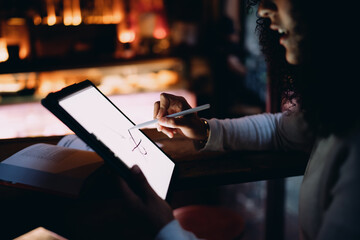 Close up of smiling woman drawing with smart stylus tool on tablet computer screen in cozy evening cafe, creative freelance illustration or distance e-learning concept portrait © BullRun