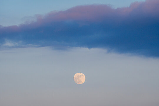 Full moon beneath dark cloud band in soft twilight sky