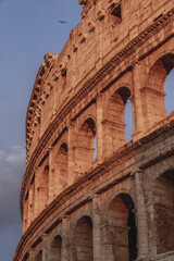 Fototapeta premium Exterior detail of the Colosseum amphitheater in Rome at golden hour showing ancient stone arches and sky