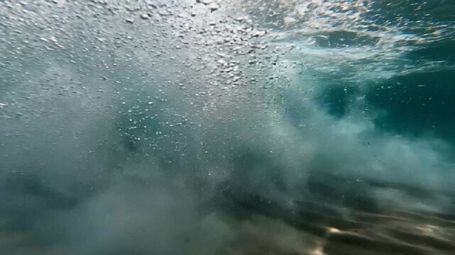 Underwater view of a powerful ocean wave breaking over clear sandy seabed