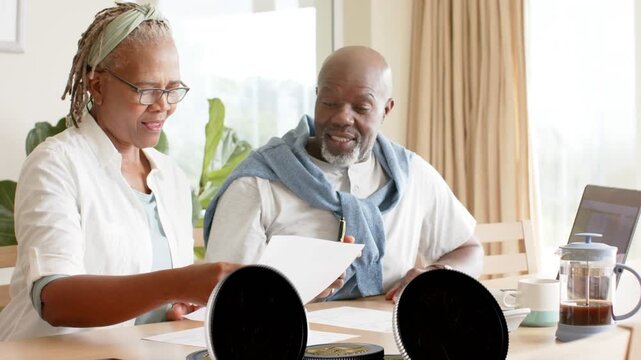 Senior couple reviewing bills at table, coin discs falling and piling over documents for finance