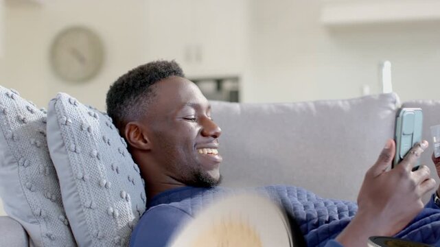 Man reclining couch scrolling phone, causing finance coins entering and piling on torso, laughing