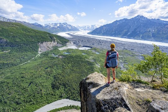 Young woman on a rocky outcrop enjoying the view, view of impressive mountain landscape with Matanuska glacier and glaciated mountain peaks, Lion's Head, Chugach Mountains, Alaska, USA