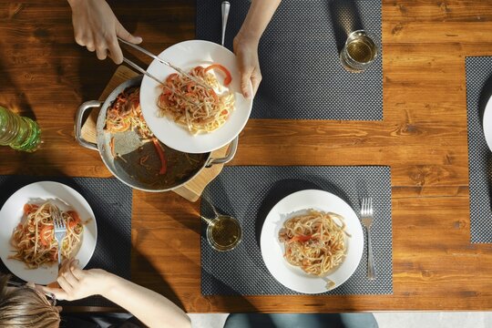 Friends gather around a wooden dining table to enjoy a healthy meal featuring fresh pasta topped with vibrant vegetables and stir fry beef. Glasses of sparkling water accompany the delicious dish