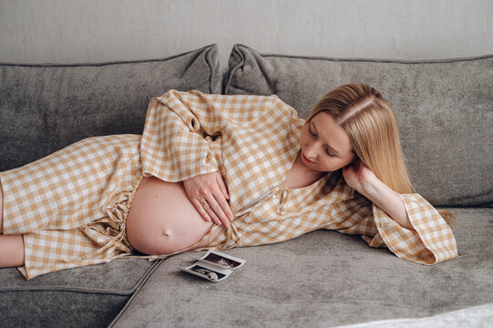 Pregnant woman relaxing with ultrasound photos at home