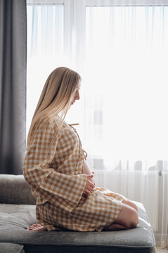 Pregnant woman relaxing on sofa by bright window at home