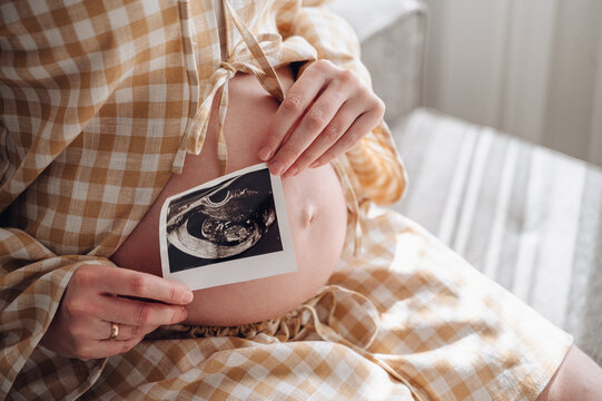 Pregnant woman relaxing on sofa holding ultrasound photo
