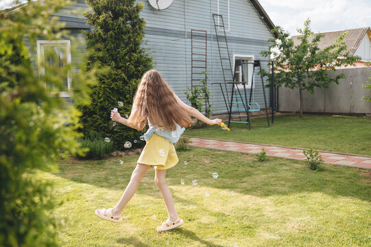 Girl chasing bubbles in sunny backyard during summer play
