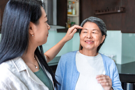 Asian daughter caring for smiling mother at home kitchen