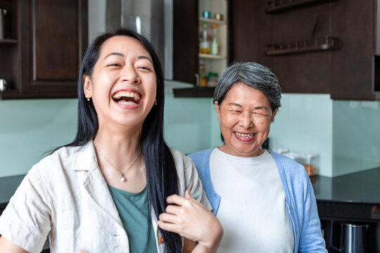 Asian mother and daughter laughing together at home kitchen