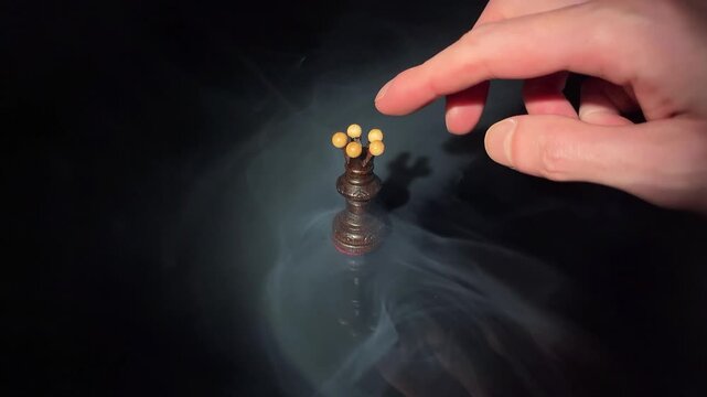 Human hand knocking over dark wooden chess queen in dramatic smoke on black background. Concept of defeat, overthrow, power, disruption and business failure.
