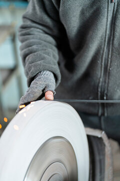 Worker grinding metal on industrial wheel with sparks
