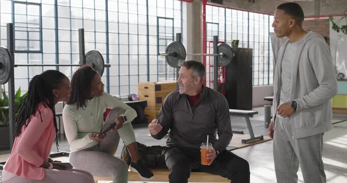 Diverse friends leaning, man speaking, pointing, tapping phone and tablet, sharing clip in loft gym