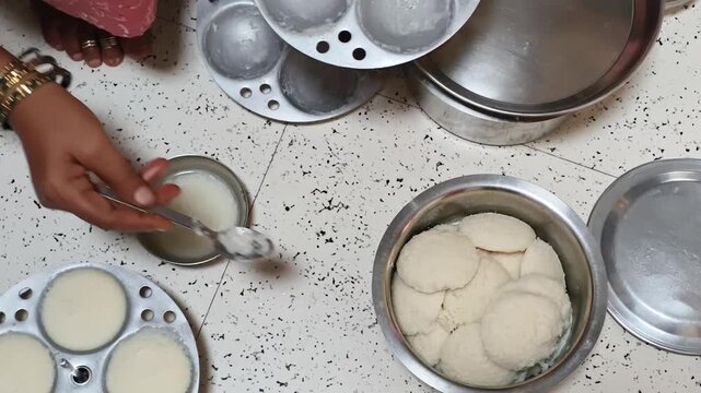 Hands removing freshly steamed idli from a traditional mold in a home kitchen, showcasing authentic South Indian cooking, homemade breakfast, healthy food, culinary tradition and family lifestyle.