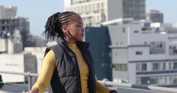 African woman walking rooftop, scanning city, turning toward metal railing, raising WOMEN sign high