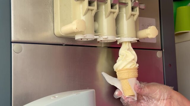 Soft serve vanilla ice cream pouring into a waffle cone from machine