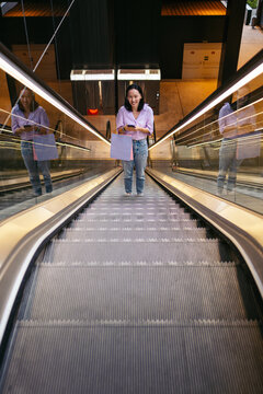 Asian woman with shopping bag on an escalator