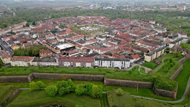 Aerial drone close view of dense terracotta rooftops with narrow alleys and hidden courtyards inside fortress walls. Urban texture detail with plazas and garden spaces within fortified citadel grid.
