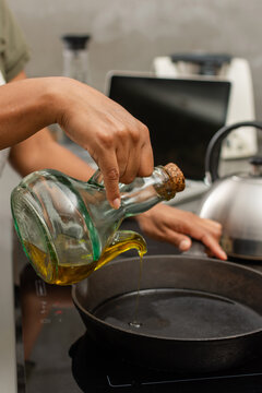 Close up of pouring olive oil into cast iron skillet with laptop in background