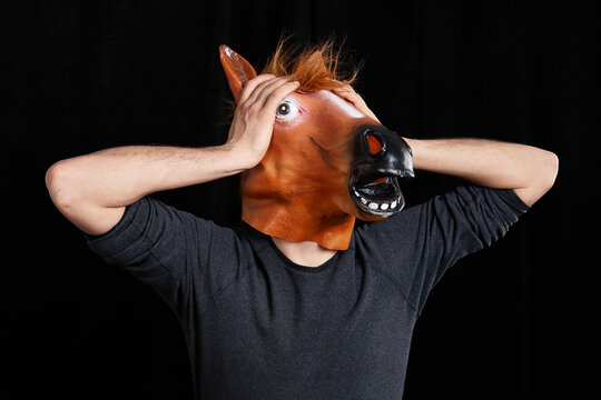 Man wearing horse mask holding head in stress isolated on black background