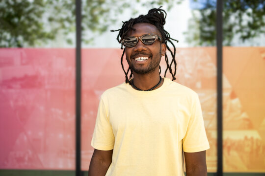 Smiling Cuban man in sunglasses standing by colorful wall