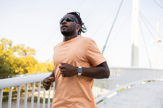 Cuban man jogging on bridge with smartwatch at sunrise