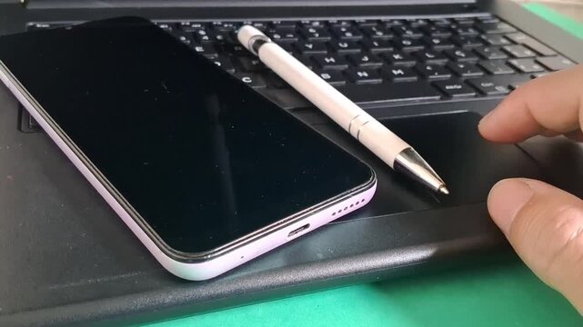 Hand using laptop trackpad near smartphone and pen video motion