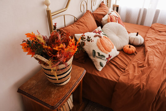 Cozy bedroom with brown bedding decorative pillows and a basket of autumn flowers