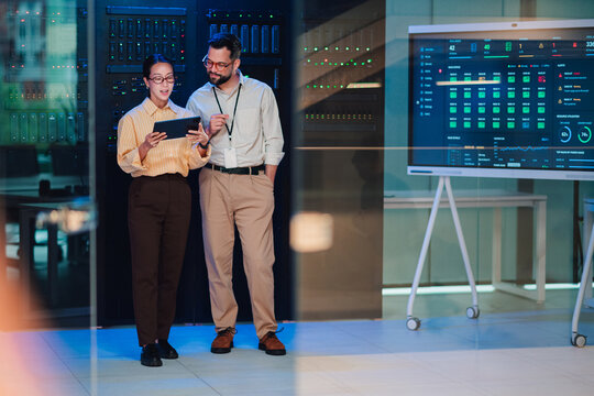 It professionals analyzing data on tablet in server room with network engineers managing cloud computing infrastructure