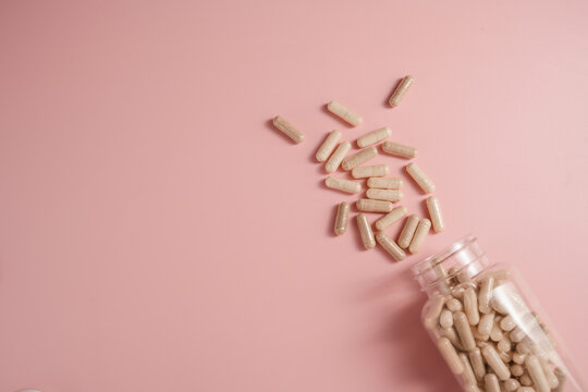 Collagen supplement capsules spilling from bottle on pink background with copy space, feminine food supplement abstract background