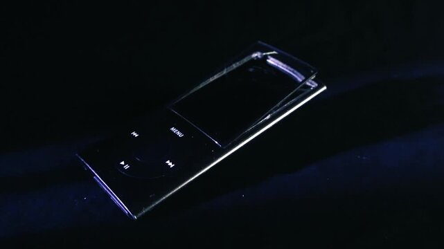 Damaged and obsolete black portable mp3 music player with a detached screen lying on a dark, textured surface, representing outdated technology and the concept of planned obsolescence