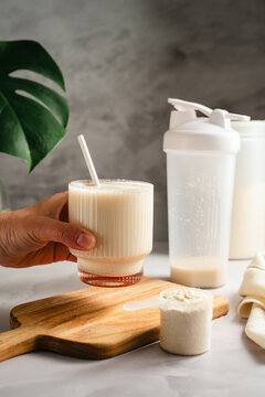 Hand holding protein shake glass with whey powder scoop, sports nutrition concept