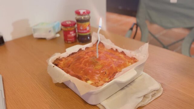 A freshly baked homemade apple pie served in a ceramic baking dish, topped with a lit birthday candle. The golden crust is warm and rustic, with sweet apples and raisins baked inside
