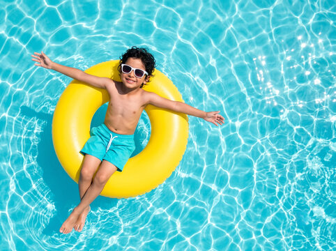 cute indian boy floating on inflatable swim ring in crystal clear swimming pool for summer holiday concept