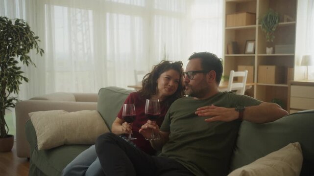 Happy caucasian couple sitting near the sofa with glasses of red wine 