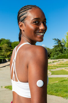 Gen Z Black woman wearing glucose sensor in sunny park