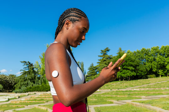 Gen Z woman checks glucose sensor data on phone outdoors