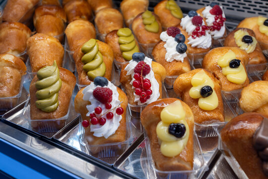 Naples, italy. December 27, 2024. Rows of traditional neapolitan baba rum cakes topped with whipped cream, berries, pistachio, and custard in a bakery display