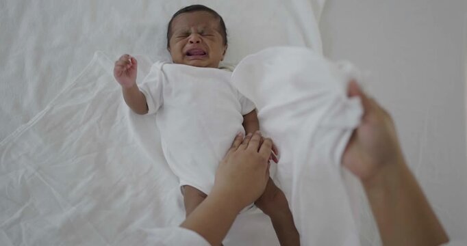 Close-up of a caregiver or mother gently change diaper swaddling a crying black African newborn baby on a bed, infant care, soothing techniques, parenting, and newborn wellness.