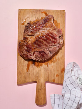 Cooked beef on wooden board with pink background