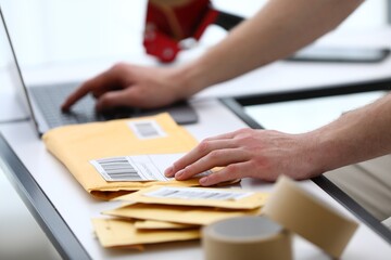 Fototapeta premium Man with postal envelopes working on laptop at table in office, closeup