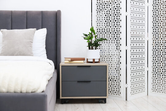 Folding screen, bedside table with decor and bed in room. Interior design