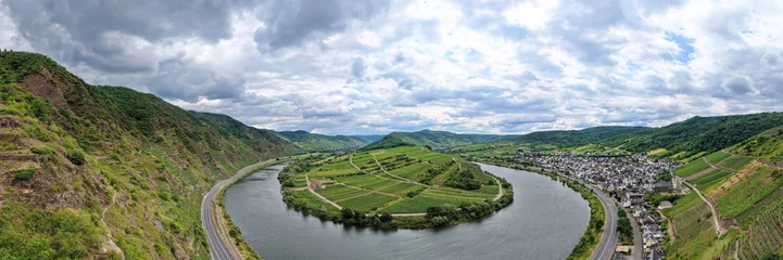 Weitwinkel-Luftaufnahme der berühmten Moselschleife mit der historischen Klosterruine Stuben auf einer von grünen Weinbergen geprägten Halbinsel unter bewölktem Himmel. © fotoping