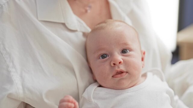 Caucasian newborn baby face with open mouth and raised hand, gazing at camera while cradled against white shirt in building; curiosity tenderness.