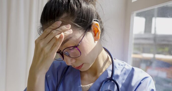 Female healthcare professional wearing scrubs and a stethoscope holding her forehead, expressing stress, fatigue, burnout, and mental pressure in a clinical setting.