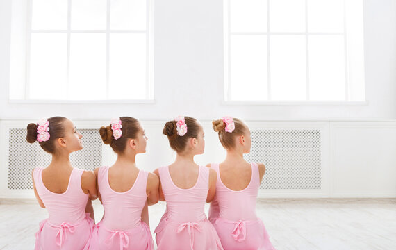 Little ballerinas in ballet studio. Group of girls having break in practice, sitting on floor, back view. Classical dance school