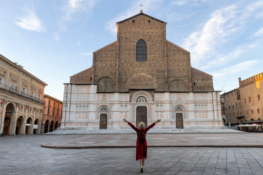 Young tourist dressed in red with arms raised in front of central square near San Petronio basilica in Bologna city - Italy