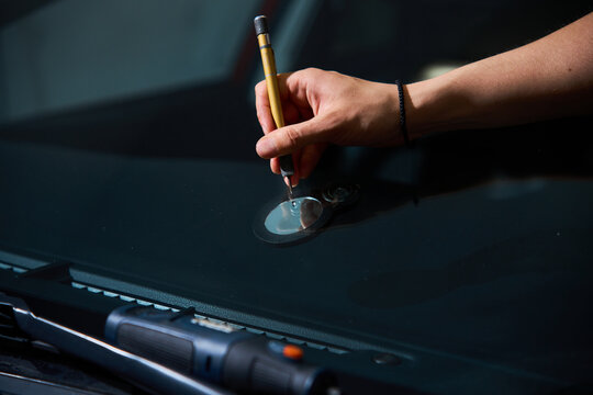 Technician uses precision scriber to clean glass damage point. Windshield repair service. Expert mechanic prepares glass damage for treatment using specialized scriber tool